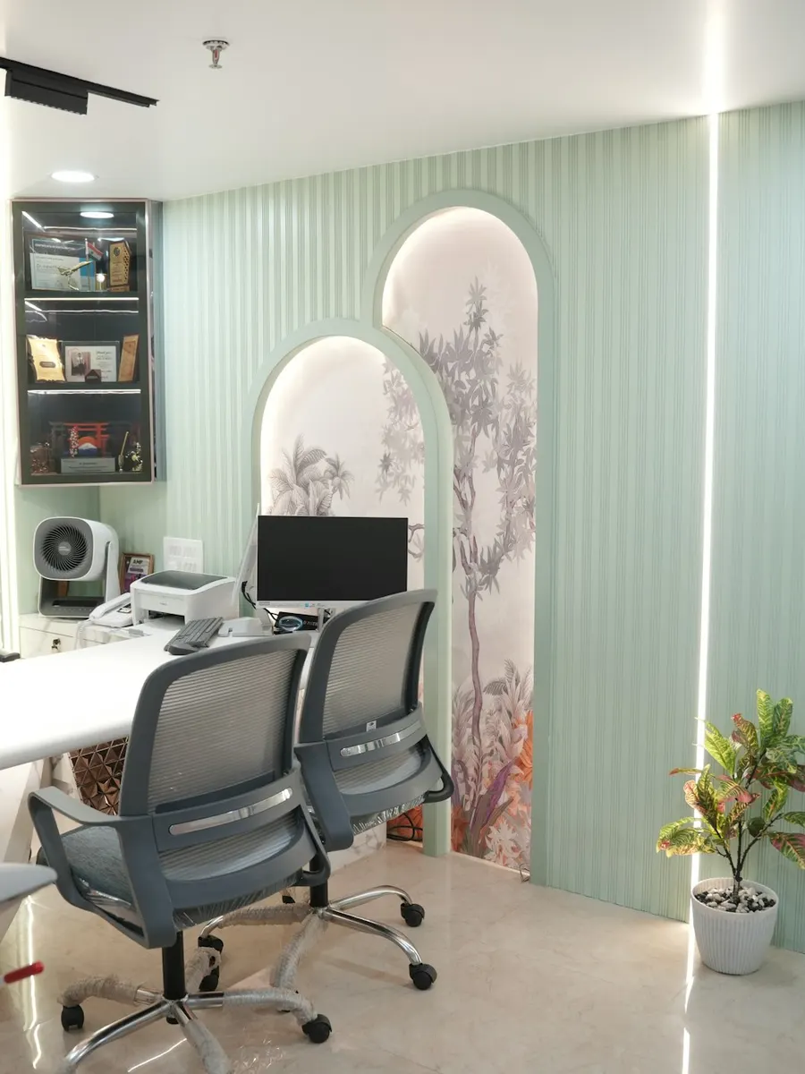 A bright consultation room with a desk, chairs and soft green walls