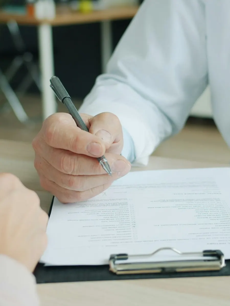 A doctor writing notes on a clipboard across the desk from a patient